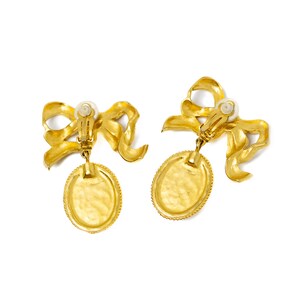 May include: A pair of gold tone clip-on earrings with a bow and oval pendant.