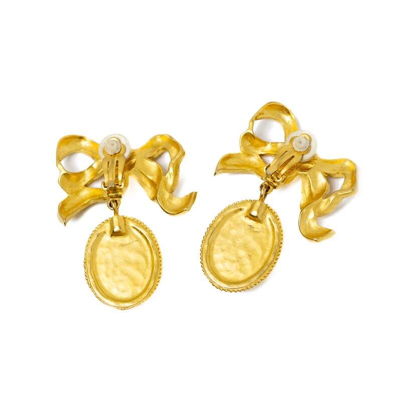 May include: A pair of gold tone clip-on earrings with a bow and oval pendant.