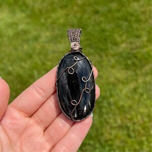 Peut inclure: Un pendentif en obsidienne noire avec un enroulement de fil de cuivre. Le fil forme un motif délicat autour de la pierre de forme ovale.
