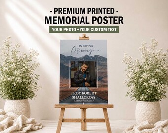 May include: A rectangular memorial poster on a wooden easel featuring a photograph of a person in a leather jacket, the text IN LOVING MEMORY, the name TROY ROBERT SHALLCROSS, and the dates 11.12.1970 - 02.01.2023 over a mountain road background.