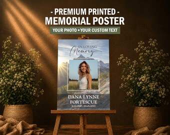 May include: A rectangular memorial poster displayed on a wooden easel. The poster features a central photograph of a person, the text IN LOVING MEMORY, the name DANA LYNNE FORTESCUE, and the dates 11.12.1940 - 02.01.2023 against a mountain landscape background.