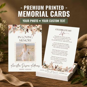 May include: Cream-colored memorial cards with floral accents and the text "PREMIUM PRINTED - MEMORIAL CARDS." One card features a photo and the words "IN LOVING MEMORY." Another card displays a poem. The cards are stacked on a wooden surface.