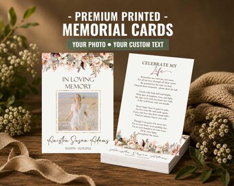 May include: Cream-colored memorial cards with floral accents and the text "PREMIUM PRINTED - MEMORIAL CARDS." One card features a photo and the words "IN LOVING MEMORY." Another card displays a poem. The cards are stacked on a wooden surface.
