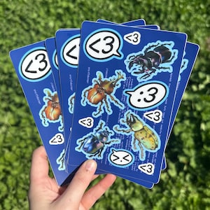 Puede incluir: Un conjunto de cinco pegatinas azules con ilustraciones de escarabajos y el texto "<3" y "snotlobster".