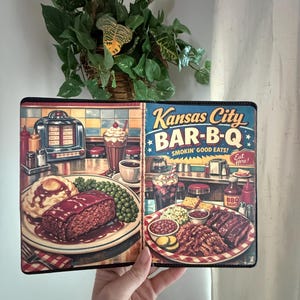 May include: A colorful, vintage-style notebook cover featuring a Kansas City Bar-B-Q design. The cover displays illustrations of classic diner food, including ribs, mashed potatoes, and milkshakes. The text "Kansas City BAR-B-Q" is prominently displayed.