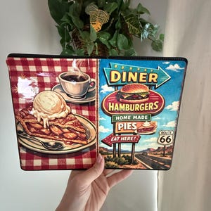 May include: A rectangular diner-themed sign featuring a slice of apple pie with ice cream, a cup of coffee, and a Route 66 sign. The sign has a red and white checkered pattern on the left side and a diner scene on the right.
