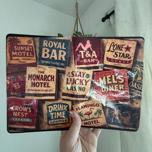 May include: A rectangular clutch featuring a collage of vintage-style motel and bar signs. The signs include "Sunset Motel," "Royal Bar," "Lone Star Lounge," and "Flamingo Motel." The clutch is held by a person.
