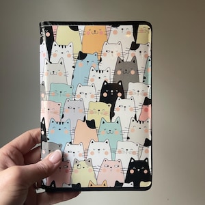 May include: A black leather passport holder with a colorful pattern of cartoon cats. The cats are in various colors, including pink, blue, yellow, and gray.