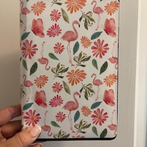 May include: A rectangular case with a white background, featuring a repeating pattern of pink flamingos, butterflies, and flowers in shades of pink, orange, and green. The case has a black border.
