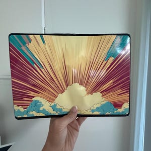 May include: A rectangular passport holder featuring a graphic illustration of a sunrise with radiating light beams in shades of yellow and orange, set against a deep magenta background with stylized blue and white clouds along the bottom edge.