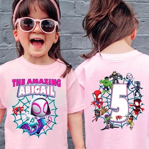 May include: Pink t-shirts with a Spider-Gwen theme. The front of the shirt has the text "THE AMAZING ABIGAIL" above a Spider-Gwen graphic in a web. The back features a large number 5 surrounded by various superhero characters.