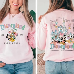 Puede incluir: Sudadera rosa con un gr&aacute;fico de Mickey Mouse y sus amigos frente al castillo de Disneyland. El texto "Disneyland Est. 1955 California" est&aacute; impreso en la parte delantera de la sudadera. La parte posterior de la sudadera tiene un gr&aacute;fico de Mickey Mouse y sus amigos frente al castillo de Disneyland con el texto "Disneyland Est. 1955".