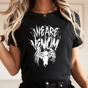 May include: Black t-shirt with the white text "WE ARE VENOM" in a stylized font, along with a white graphic of Venom's face and spider emblem. The shirt has short sleeves and a crew neck.
