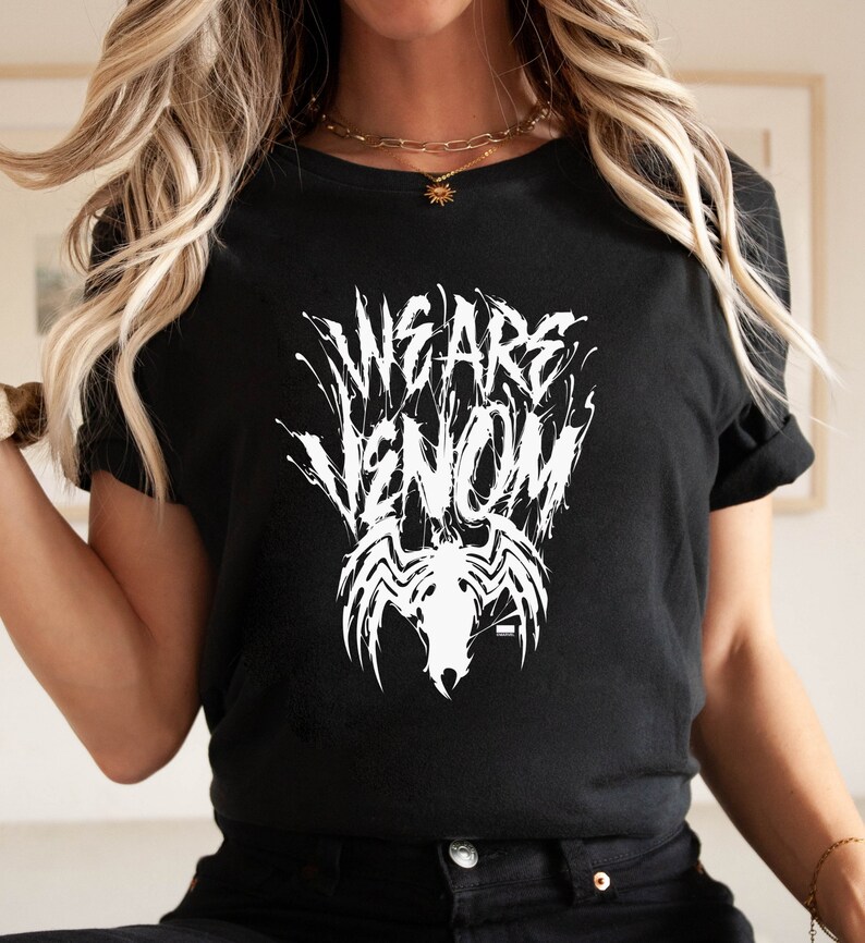 May include: Black t-shirt with the white text "WE ARE VENOM" in a stylized font, along with a white graphic of Venom's face and spider emblem. The shirt has short sleeves and a crew neck.