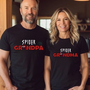 Puede incluir: Una pareja lleva camisetas negras con un gr&aacute;fico de Spider-Man rojo y blanco. La camiseta del hombre dice "Spider Grandpa" y la camiseta de la mujer dice "Spider Grandma".