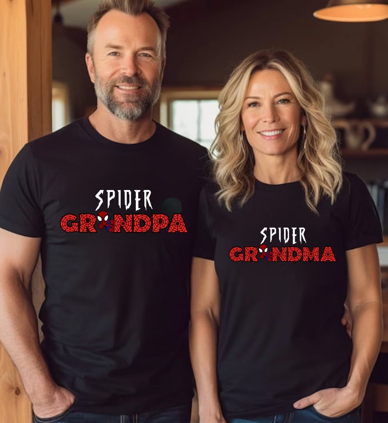 Puede incluir: Una pareja lleva camisetas negras con un gr&aacute;fico de Spider-Man rojo y blanco. La camiseta del hombre dice "Spider Grandpa" y la camiseta de la mujer dice "Spider Grandma".