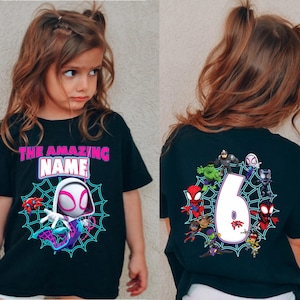 Op de afbeelding: Zwart T-shirt met een Spider-Gwen afbeelding en de tekst "THE AMAZING NAME" in roze en wit. De achterkant van het shirt toont het nummer 6 omringd door Spider-Man personages. Een leuk en kleurrijk ontwerp voor kinderen.