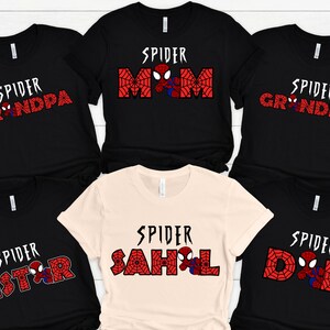 May include: Six black t-shirts with red and white spider-man themed designs. The shirts have the text "Spider Mom", "Spider Dad", "Spider Grandma", "Spider Grandpa", "Spider Sister", and "Spider Sahl" printed on them.