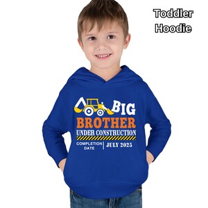 May include: A royal blue toddler hoodie with the words "BIG BROTHER UNDER CONSTRUCTION" in white and orange, along with a yellow construction vehicle graphic. The completion date is July 2025.