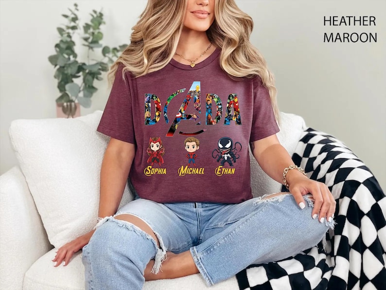 Peut inclure: Un t-shirt &agrave; manches courtes couleur bordeaux chin&eacute; avec le texte DADA rempli de motifs de super-h&eacute;ros. Sous le texte se trouvent trois personnages de style chibi avec les pr&eacute;noms Sophia, Michael et Ethan imprim&eacute;s en jaune en dessous.