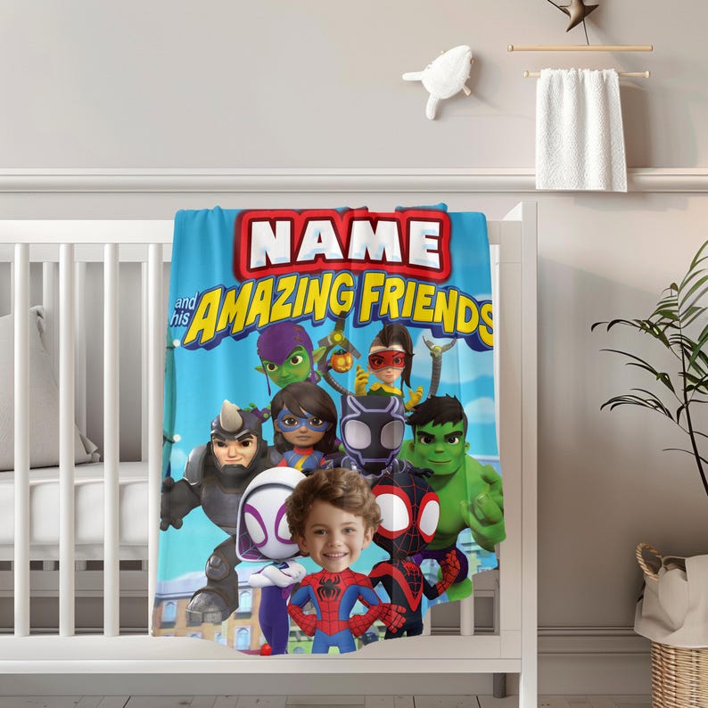 May include: A blue blanket with the text "NAME and his AMAZING FRIENDS" and cartoon superhero characters. The blanket is draped over a white crib. The blanket features a child's face in the center.