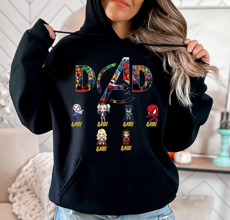 Peut inclure: Un sweat &agrave; capuche noir avec le mot DAD en grandes lettres remplies de divers graphismes de super-h&eacute;ros. Sous le texte se trouvent six petites figurines de super-h&eacute;ros style chibi, chacune avec le mot NAME imprim&eacute; en jaune en dessous.