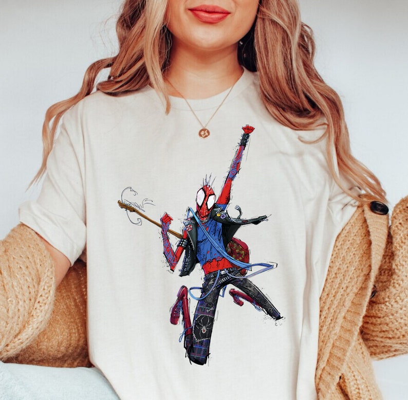 May include: A white t-shirt with a graphic of a red and blue Spider-Man character playing a guitar. The character is wearing a blue jacket and black pants.