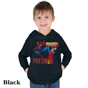 Puede incluir: Sudadera con capucha negra con un gr&aacute;fico de Spiderman en estilo de c&oacute;mic. El gr&aacute;fico incluye el texto "Amazing Spiderman" y el n&uacute;mero "7". El texto "Paxton" tambi&eacute;n est&aacute; incluido en el gr&aacute;fico.