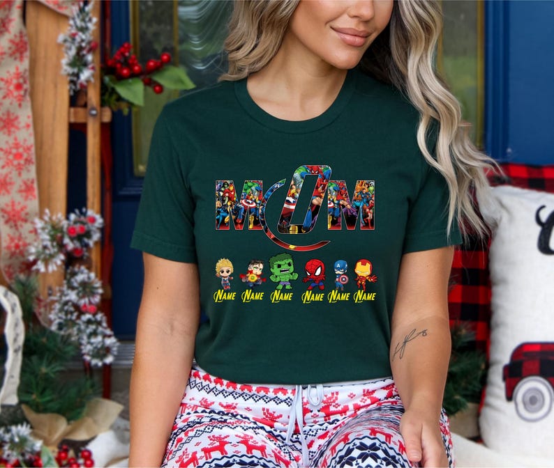 Peut inclure: Un t-shirt &agrave; manches courtes vert fonc&eacute; avec le mot MOM &eacute;crit dans une police de style collage de super-h&eacute;ros color&eacute;s. Sous le texte se trouvent six petites figurines de super-h&eacute;ros avec le mot Name imprim&eacute; en jaune en dessous.