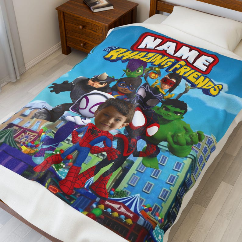 May include: A blue blanket featuring a group of cartoon superheroes with the text "NAME Amazing Friends". The blanket has a personalized photo of a child's face in the center. The blanket is on a white bed.