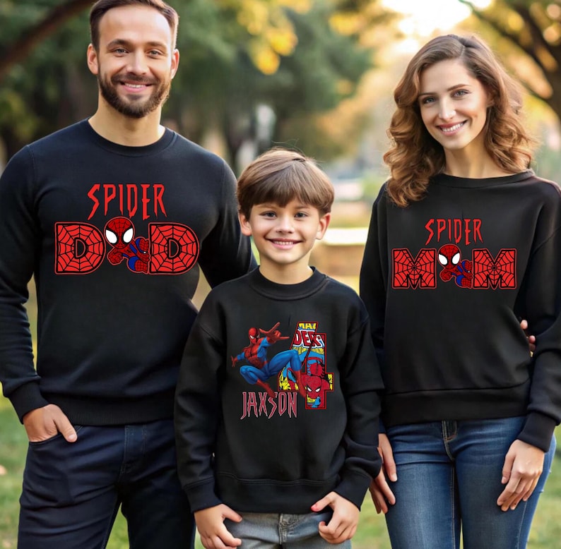 Puede incluir: Un conjunto de sudaderas negras a juego para la familia con tem&aacute;tica de Spider-Man. Las sudaderas para adultos dicen "Spider Dad" y "Spider Mom" con un dibujo animado de Spider-Man en un dise&ntilde;o de telara&ntilde;a. La sudadera para ni&ntilde;os tiene un gr&aacute;fico de Spider-Man m&aacute;s grande y el texto "That's My Super Hero" y "Jaxson".