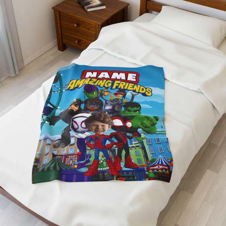 May include: A blue blanket featuring a group of cartoon superheroes with the text "NAME AMAZING FRIENDS". The blanket is decorated with a cityscape and a blue sky background. The blanket is folded on a white bed.