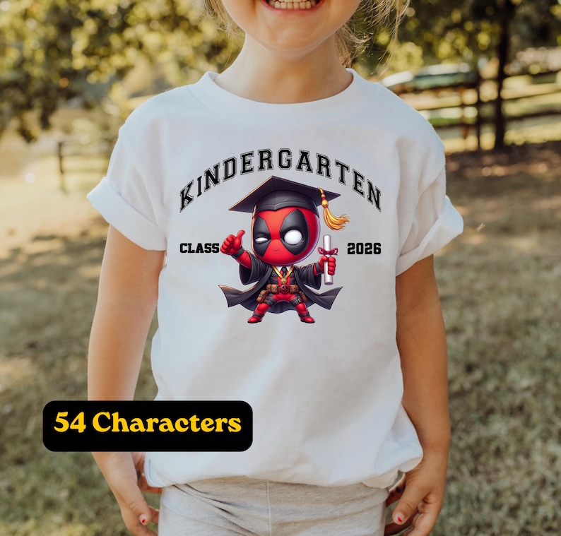 Puede incluir: Una camiseta blanca con un gr&aacute;fico de un personaje rojo y negro con birrete y toga de graduaci&oacute;n, sosteniendo un diploma. El texto dice "KINDERGARTEN" en un arco arriba y "CLASS 2026" a los lados de la ilustraci&oacute;n del personaje.