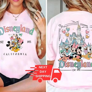 Puede incluir: Camiseta rosa con un gr&aacute;fico de Disneyland. La parte delantera de la camiseta presenta un grupo de personajes de Disney, incluidos Mickey Mouse, Minnie Mouse, Donald Duck y Goofy. La parte trasera de la camiseta presenta un gr&aacute;fico del castillo de Disneyland con el texto "Disneyland Est. 1955".
