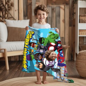 May include: A blue blanket featuring various Marvel characters, including Hulk, Spider-Man, and others. The blanket has the words "Amazing Friends" in yellow and blue. A child is holding the blanket.