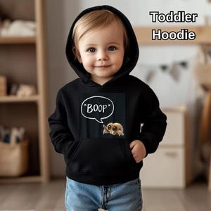 Puede incluir: Sudadera con capucha negra para ni&ntilde;os peque&ntilde;os con bolsillo delantero y capucha. La sudadera con capucha presenta un gr&aacute;fico de una ara&ntilde;a de dibujos animados con la palabra "BOOP" en una burbuja. El texto "Toddler Hoodie" est&aacute; en la esquina superior derecha.