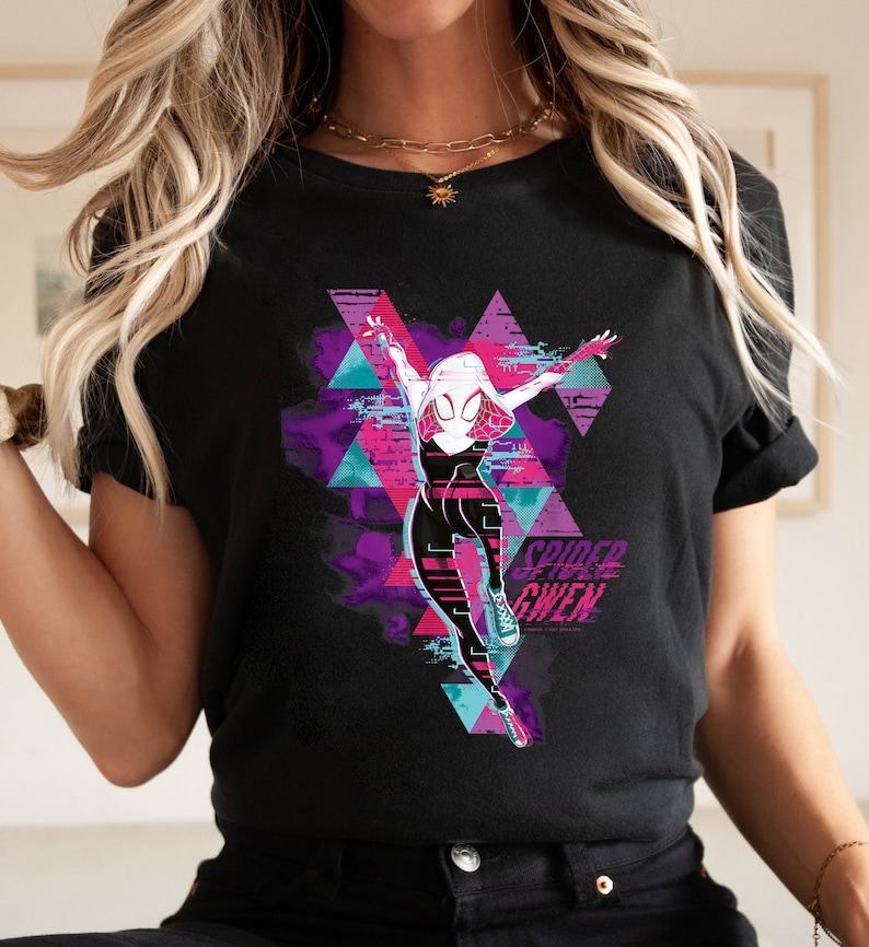 May include: Black t-shirt featuring a graphic of Spider-Gwen in a dynamic pose, set against a backdrop of purple, pink, and teal geometric shapes. The words "Spider-Gwen" are printed in a stylized font.