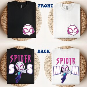 Op de afbeelding: Zwarte en witte t-shirts met een Spider-Gwen ontwerp. De voorkant van de shirts toont het masker van het personage, terwijl de achterkant de woorden "Spider-SOS" en "Spider-Mom" met een afbeelding van het personage toont. De shirts worden gepresenteerd op een geweven achtergrond.