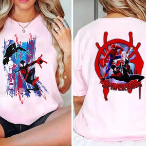 May include: Pink t-shirt featuring Spider-Man characters. The front graphic shows Spider-Man in action with a cityscape backdrop in red, white, and blue. The back displays a red Spider-Man logo with multiple Spider-Man characters and the word "SPIDER-MAN".