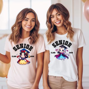 Puede incluir: Una camiseta rosa claro y una camiseta blanca, cada una con un gr&aacute;fico de un personaje de dibujos animados con birrete y toga de graduaci&oacute;n. El texto SENIOR CLASS 2026 est&aacute; impreso sobre y al lado de los personajes en fuente negra negrita.