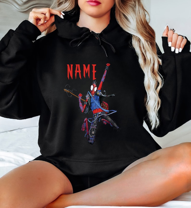 May include: Black hoodie with a graphic of a red and blue Spider-Man character playing a guitar. The text "NAME" is printed in red above the graphic.