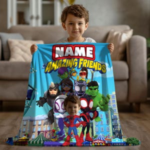 May include: A blue blanket featuring the text "NAME and his AMAZING FRIENDS" with cartoon superhero characters. The blanket is held by a young child. The blanket has a cityscape design at the bottom.