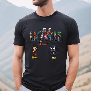 Peut inclure: Un t-shirt noir &agrave; manches courtes avec le mot UNCLE en grandes lettres remplies d'images de super-h&eacute;ros. Sous le texte se trouvent deux illustrations de personnages de style chibi &eacute;tiquet&eacute;es Michele et Max en &eacute;criture cursive jaune.