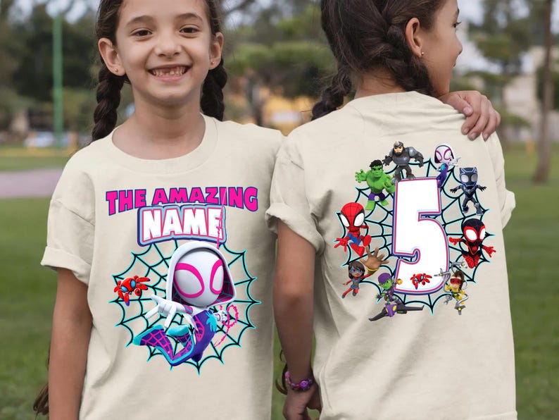 Op de afbeelding: Beige t-shirt met een Spider-Gwen-afbeelding, een webontwerp en de tekst "THE AMAZING NAME". De achterkant van het shirt toont het nummer 5 omringd door superhelden.