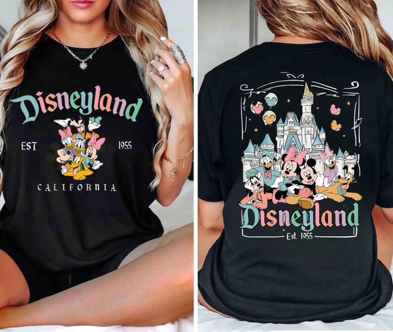 Puede incluir: Camiseta negra con un gr&aacute;fico de Disneyland colorido en la parte delantera y trasera. El gr&aacute;fico delantero presenta a Mickey Mouse y sus amigos, con el texto "Disneyland EST 1955 CALIFORNIA". El gr&aacute;fico trasero presenta a Mickey Mouse y sus amigos frente al castillo de Disneyland, con el texto "Disneyland - Est. 1955 - ".