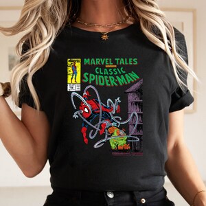 May include: Black t-shirt featuring a comic book cover design. The graphic includes the text "MARVEL TALES CLASSIC SPIDER-MAN" with an illustration of Spider-Man in action. The comic book cover art is in vibrant colors.