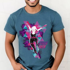 May include: A teal short-sleeved t-shirt featuring a graphic of Spider-Gwen in a dynamic pose. The design includes a pink, purple, and teal geometric background with the text "Spider-Gwen" in white. The shirt is made of a soft material.
