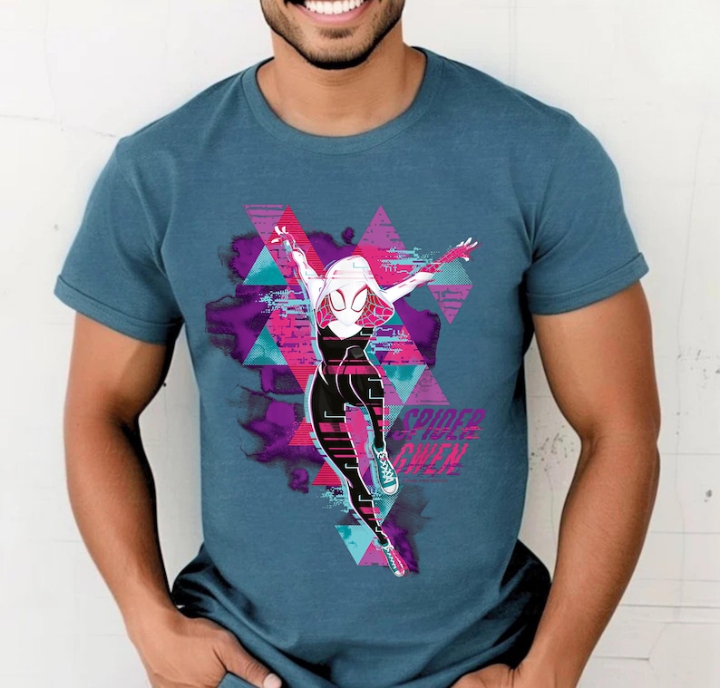 May include: A teal short-sleeved t-shirt featuring a graphic of Spider-Gwen in a dynamic pose. The design includes a pink, purple, and teal geometric background with the text "Spider-Gwen" in white. The shirt is made of a soft material.