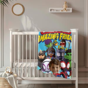 May include: A blue blanket with the words "AMAZING FRIENDS" in yellow and a group of cartoon superheroes. The blanket is draped over a white crib. A child's face is superimposed on the blanket.