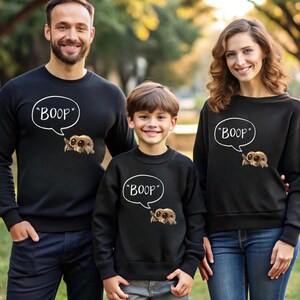 Puede incluir: Sudaderas negras con un dibujo de ara&ntilde;a de dibujos animados y la palabra "BOOP" en una burbuja de di&aacute;logo. La imagen muestra a una familia con sudaderas a juego, ideal para una salida familiar o un evento tem&aacute;tico.